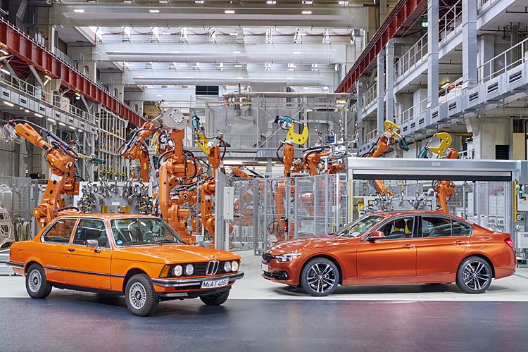 BMW 3er E21 und BMW 3er F30 in orangener Lackierung vor orangefarbenen Produktionsrobotern