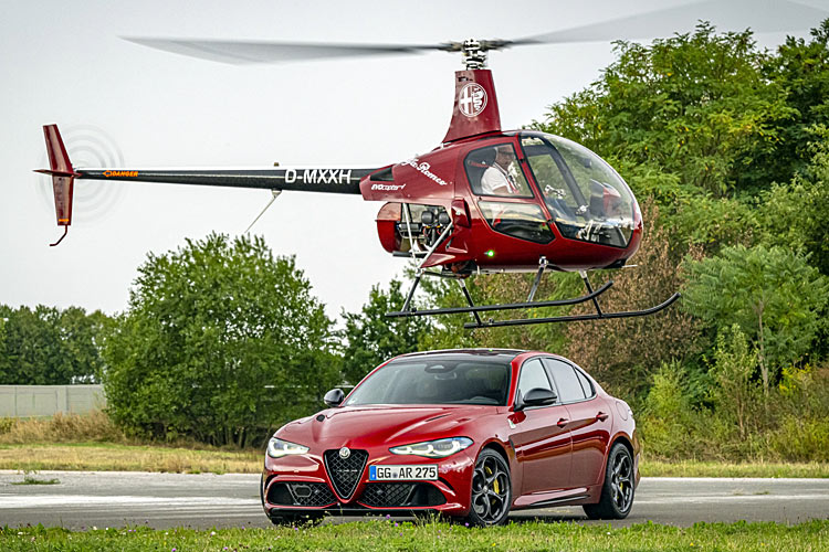 Ein roter Alfa Romeo Giulia Quadrifoglio, darüber fliuegt ein Ultraleicht-Hubschrauber im Alfa-Design