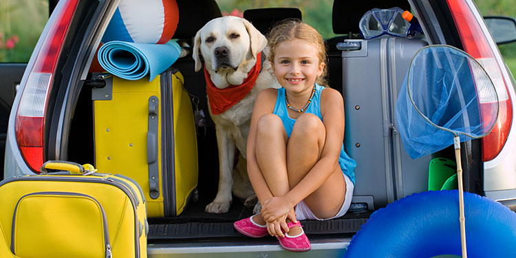 Mädchen mit Hund und Urlaubsgepäck im Kofferraum